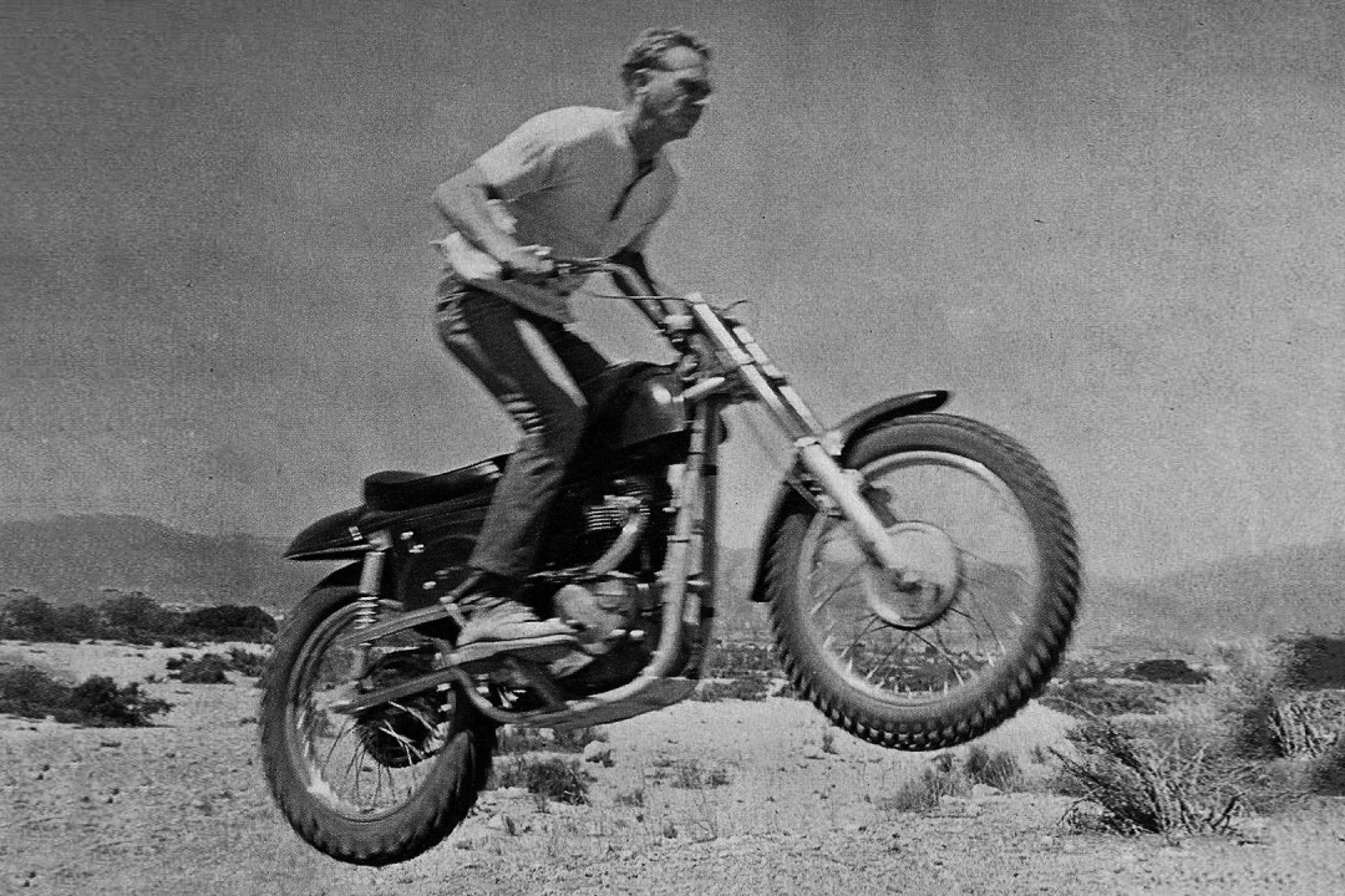 A black & white photo of Steve McQueen jumping his Metisse Desert Racer in the Californian Desert in the 1960s.