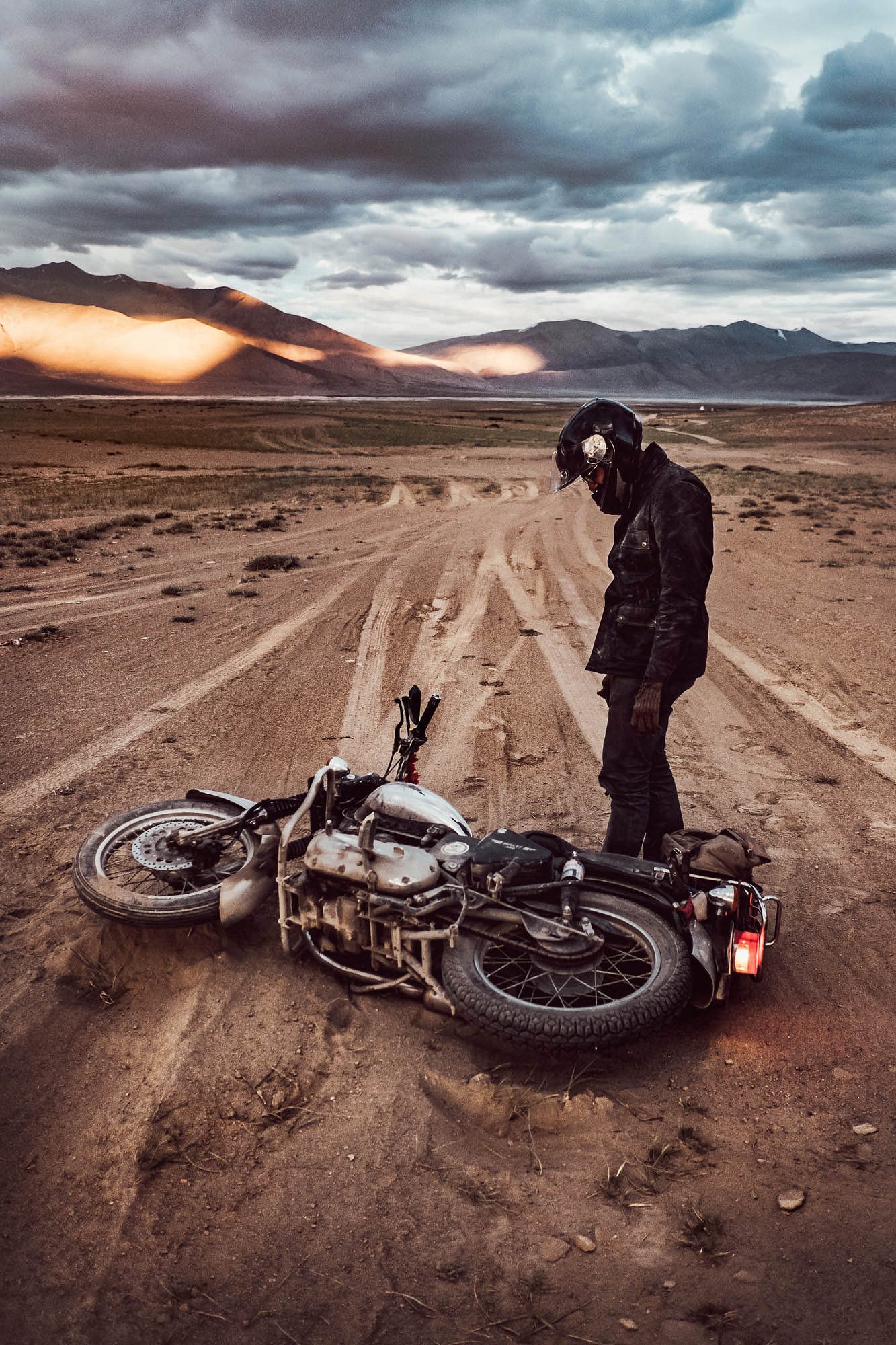 A motorcycle rider looks down at his fallen bike on a majestic road in the Rajasthan desert