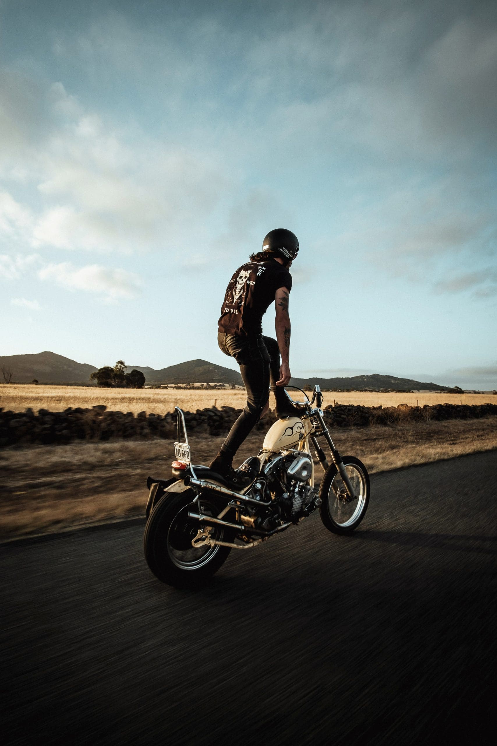 A Harley chopper rider in rural Australia stands upright on his bike as it travels down the road
