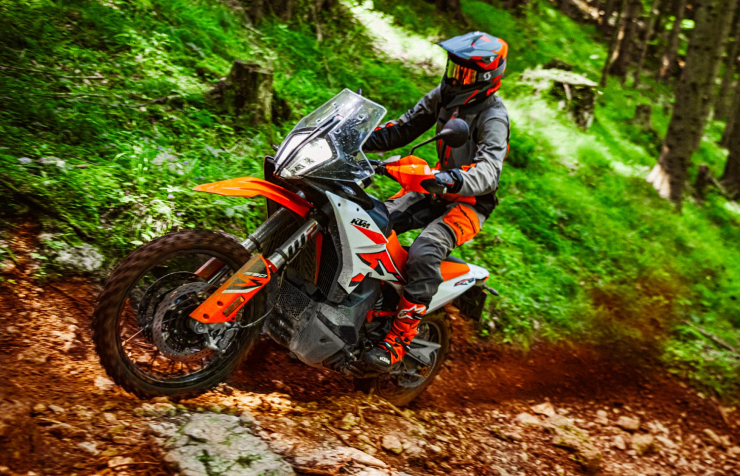 A KTM 890 R Adventure motorcycle climbs up a dirt path in a forest