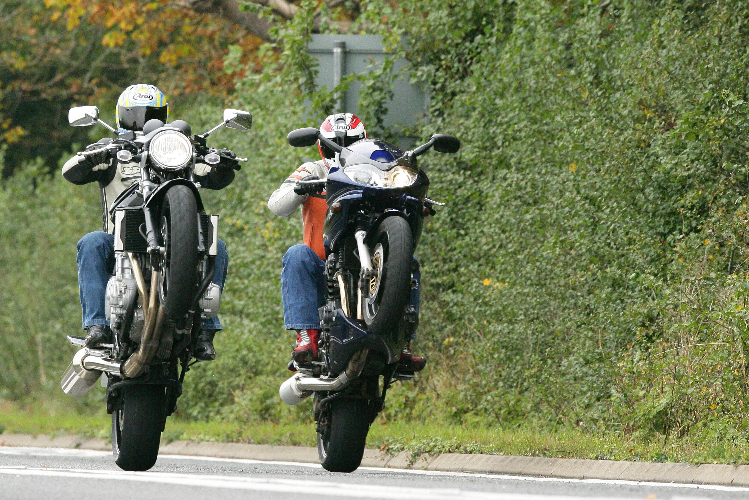 Two motorcyclists perform wheelies on motorcycles